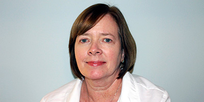 Portrait of a faculty member against a neutral background, wearing a white blazer and looking at the camera.